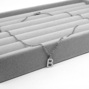 Macro shot of silver stainless steel necklace with letter B pendant on velvet tray