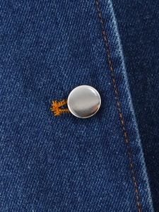 Gros plan du denim bleu foncé avec bouton en métal argenté et coutures orange contrastées