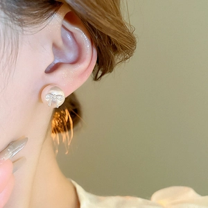 Close-up of elegant bow pearl stud earring with small crystals worn on ear