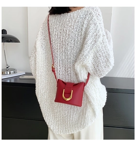 Red leather crossbody bag with gold buckle worn by model in a stylish white knit sweater
