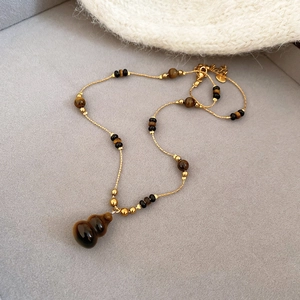 Macro shot of gold necklace with brown tiger eye gourd pendant and delicate beads