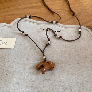 Vue détaillée du pendentif chien marron et des perles métalliques sur le collier fin