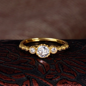Lace hollowed gold ring with three clear crystals on dark leather surface
