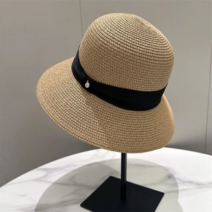 Close-up of a women's woven straw sun hat with a black ribbon and metal accent on a stand