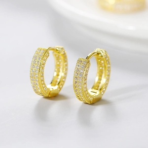 Macro shot of gold huggie earrings with micro-pave cubic zirconia on gray background
