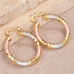 Three-tone faceted hoop earrings in gold silver and rose gold on a stone background