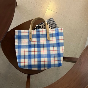 Blue plaid canvas tote bag with brown leather handles placed on a wooden chair
