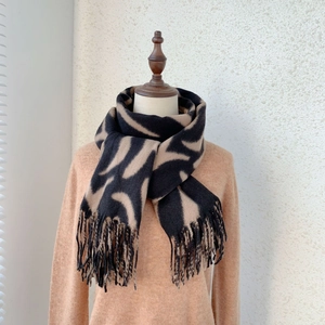 Detail of soft cashmere blend scarf featuring black and beige animal patterns and fringe
