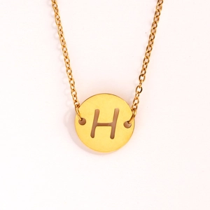 Détail macro du pendentif rond en acier inoxydable doré avec lettre H ajourée