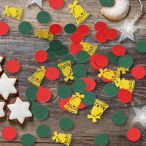 Close-up of red and green circle confetti with golden glitter bell shapes on wood background