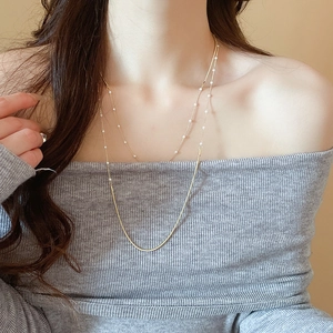 Close-up of double-layer gold necklace with small pearls and a sleek snake chain on neck
