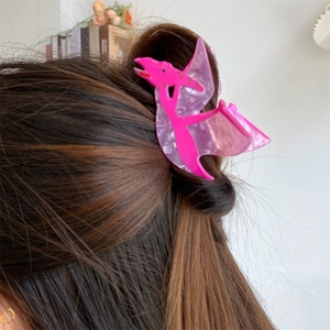 Detail of a pink pterosaur dinosaur acrylic hair claw clip worn on a bun hairstyle