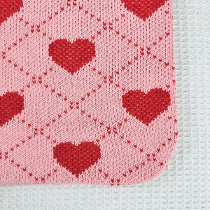 Macro shot of pink knitted fabric with red heart patterns and diamond weave detail