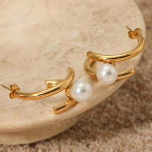 Golden C-shaped stainless steel earrings with white pearls on a natural stone background