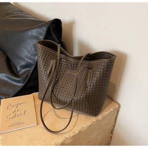 Detailed texture of dark brown woven PU leather tote bag on a stone pedestal with book