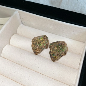 Detailed close-up of irregular resin studs with colorful gold foil in a beige jewelry box
