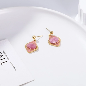 Macro detail of gold-plated leaf earrings with pink enamel in a white ceramic dish
