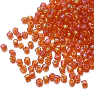 Macro shot of iridescent orange glass seed beads for jewelry making on white background