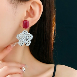 Gros plan d'une boucle d'oreille fleur avec clou carré rouge et pétales à pois noirs