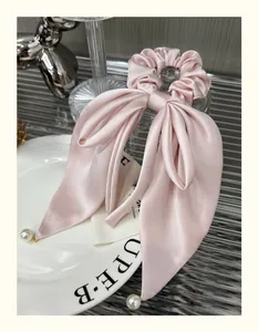 Detail of pink satin bow scrunchie with elegant ribbon and pearl pendant charms