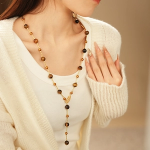 Detailed shot of tiger eye beaded necklace with a golden feather pendant on model