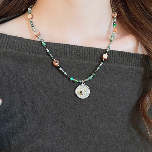 Détail du collier de perles avec pendentif soleil et lune sur un pull en maille foncé