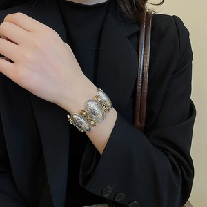 Detail of vintage two-tone relief textured metal bracelet worn with a black suit jacket