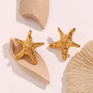 Macro detail of golden starfish stud earring with irregular texture on a coral background