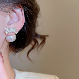 Close-up of bow knot pearl earrings with sparkling zircons worn on ear for elegant style