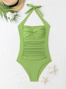 Macro view of green ruched halter swimsuit with slimming pleated details on white beach sand
