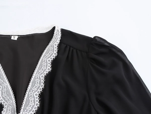 Detail of V-neckline with delicate white lace trim and puff sleeves on black chiffon dress