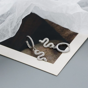 Detail of silver snake hoop earrings with white zircon crystals on artistic background
