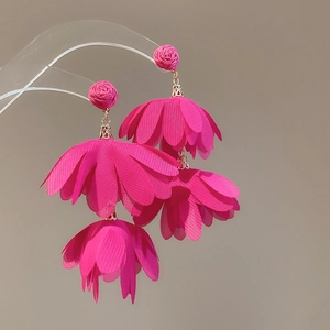 Detail of vibrant pink layered fabric flower tassel earrings on a display stand