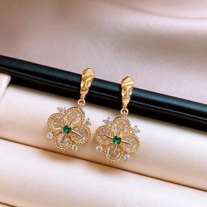 Macro detail of French vintage hollow flower earrings with green crystals and gold finish