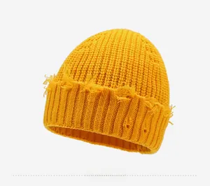 Détail du bonnet en maille jaune vif avec trous usés et bords effilochés de style urbain
