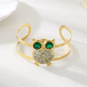 Detailed view of owl-shaped golden open bracelet with green gemstone eyes and marble inlay