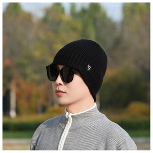 Close-up of black ribbed knit beanie with small logo label on a model in outdoor setting