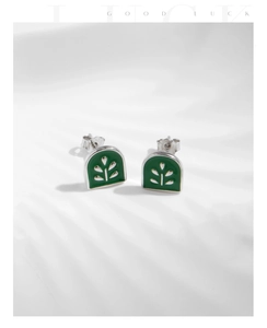 Close-up of S925 silver stud earrings with green enamel and leaf patterns on fabric