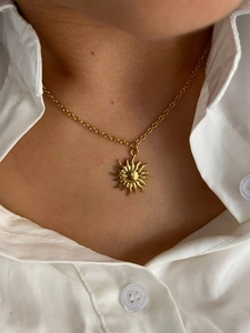 Detailed view of 18K gold plated sun pendant necklace worn on a model with white shirt