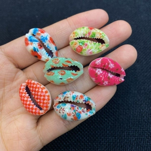 Hand holding colorful painted natural cowrie shells for DIY jewelry making
