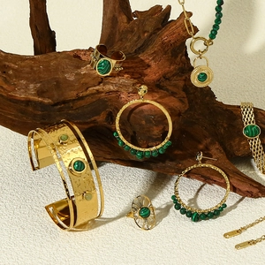 Close-up of 18k gold jewelry set with green malachite stones on textured wood