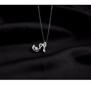 Macro shot of silver letter A pendant featuring a sparkling zircon on black silk
