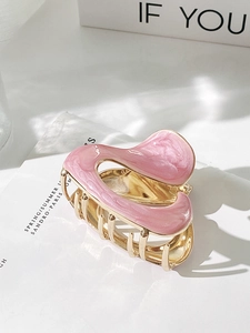 Top view of pink pearlescent enamel hair claw clip with golden metal teeth on paper