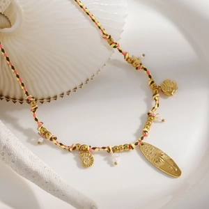 Detail of hand-woven rope necklace with shell charms and pearls on white ceramic plate