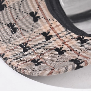 Detailed close-up of khaki plaid fabric with small black bow pattern and ribbon edging