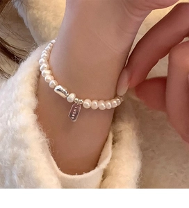 Detailed macro view of white freshwater pearls and silver Lucky charm bracelet on wrist
