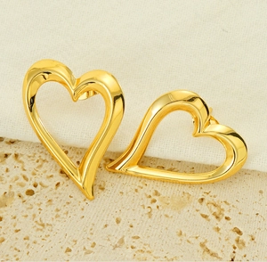 Macro di orecchini a cuore cavo placcati oro 18K su sfondo di pietra beige