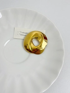 Artistic gold twisted circular brooch on a minimalist white ceramic plate with a card