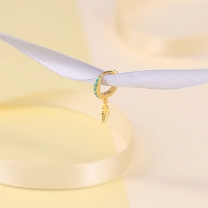Macro view of a gold boho hoop earring featuring turquoise beads and a delicate feather charm