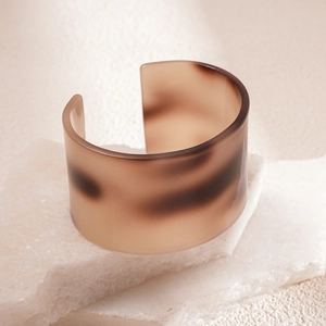 Detail of wide open cuff bracelet featuring amber tortoiseshell ink patterns and polished finish